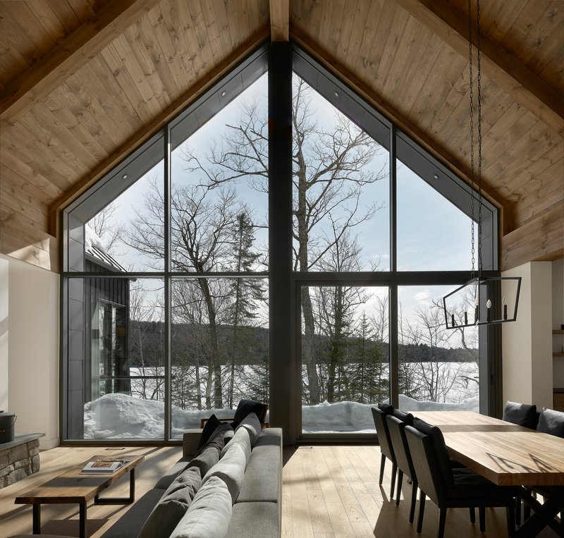 Floor to ceiling glazed gable wall framing bare winter trees and a frozen lake beyond