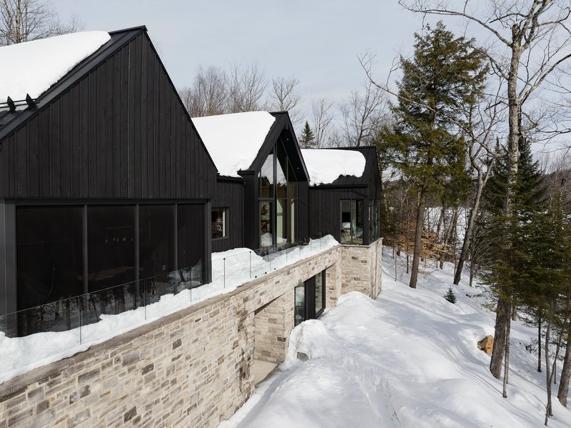 Exterior view of the black timber cladding and stone base terrace with snow on the sloped site