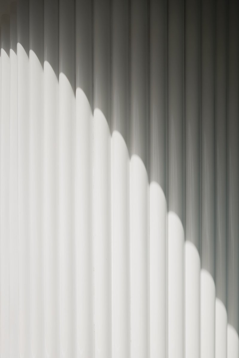 Diagonal shadow pattern cast across white vertical slat wall in natural daylight