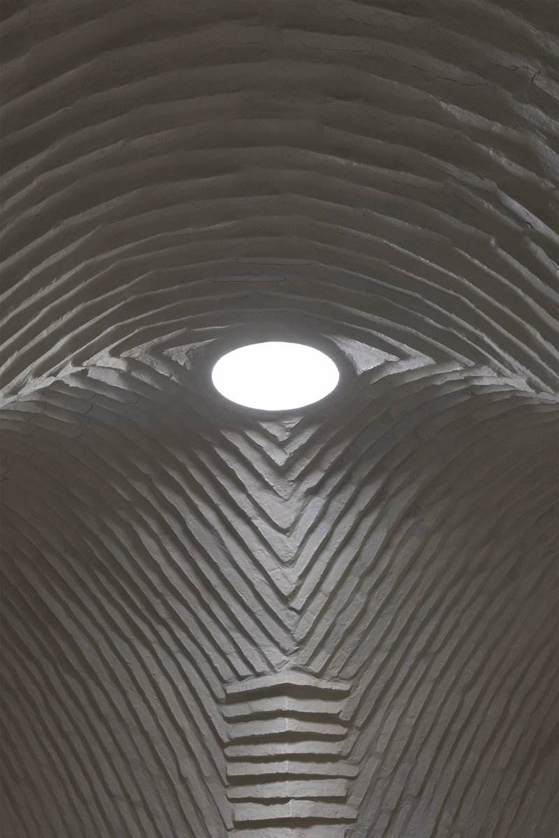Looking up at circular skylight set into ribbed concrete vault with chevron junction