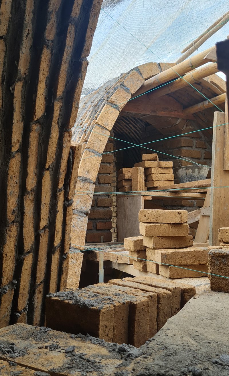 Arched brick vault under construction with timber formwork and stacked adobe bricks in sunlight