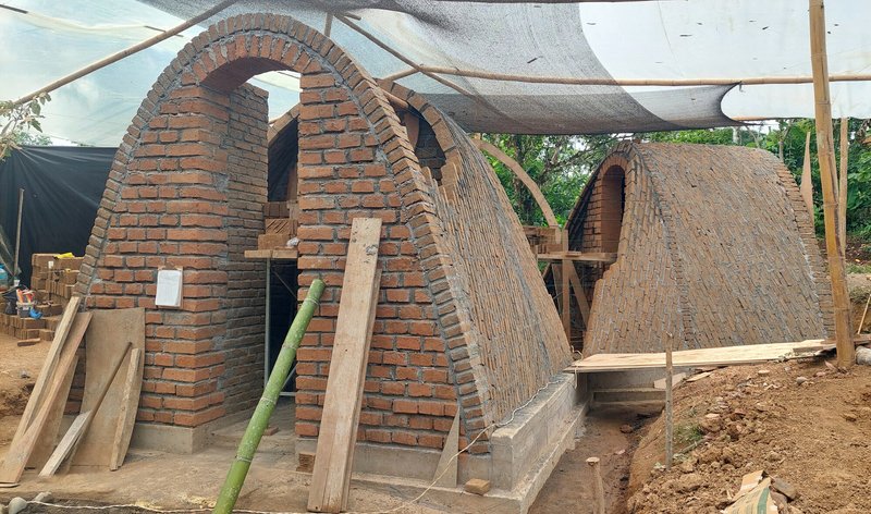 Pair of catenary brick arches with timber bracing under a mesh shade structure