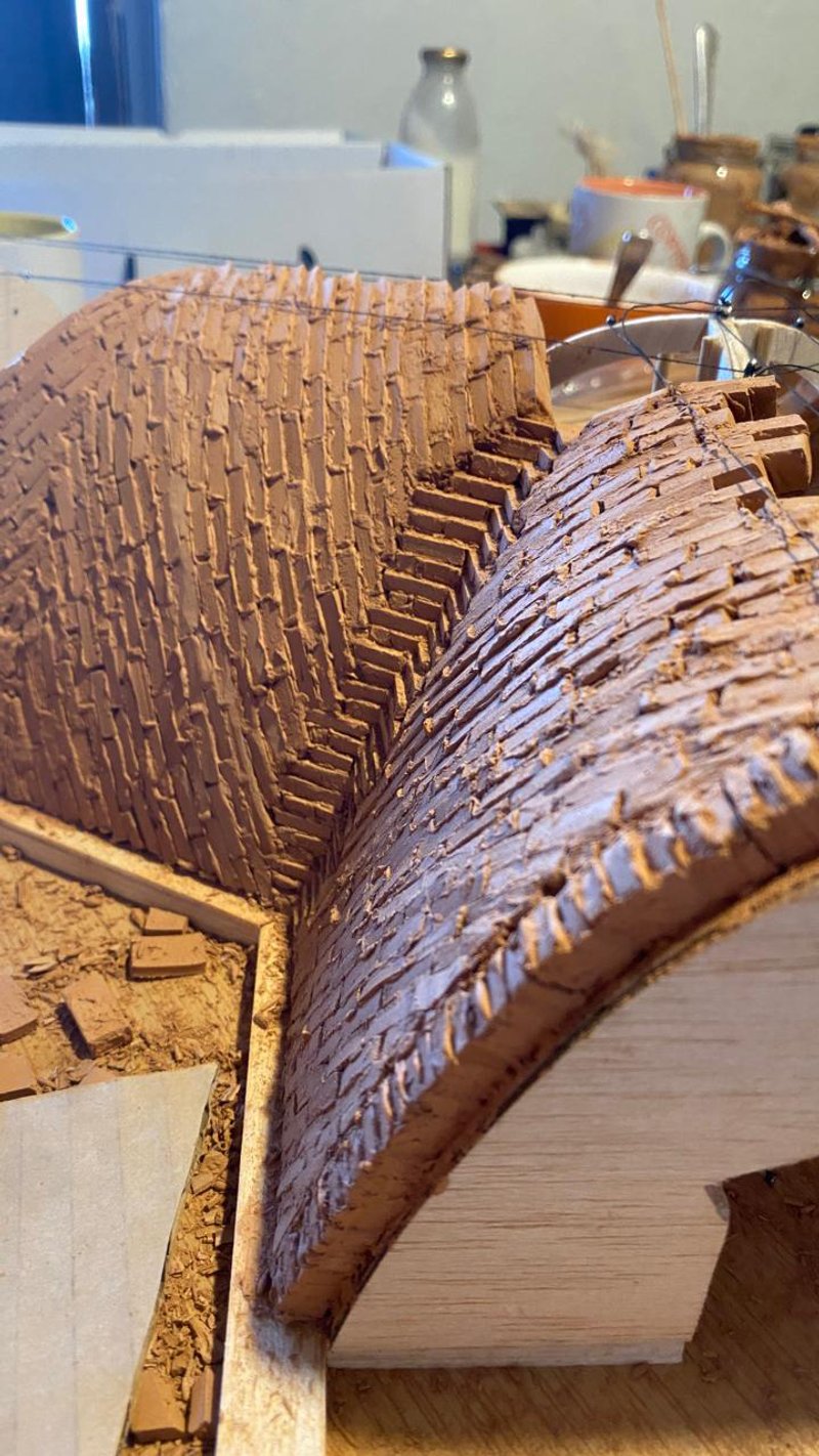 Physical model of layered timber vault with stacked plywood ribs forming a curved structural section in workshop