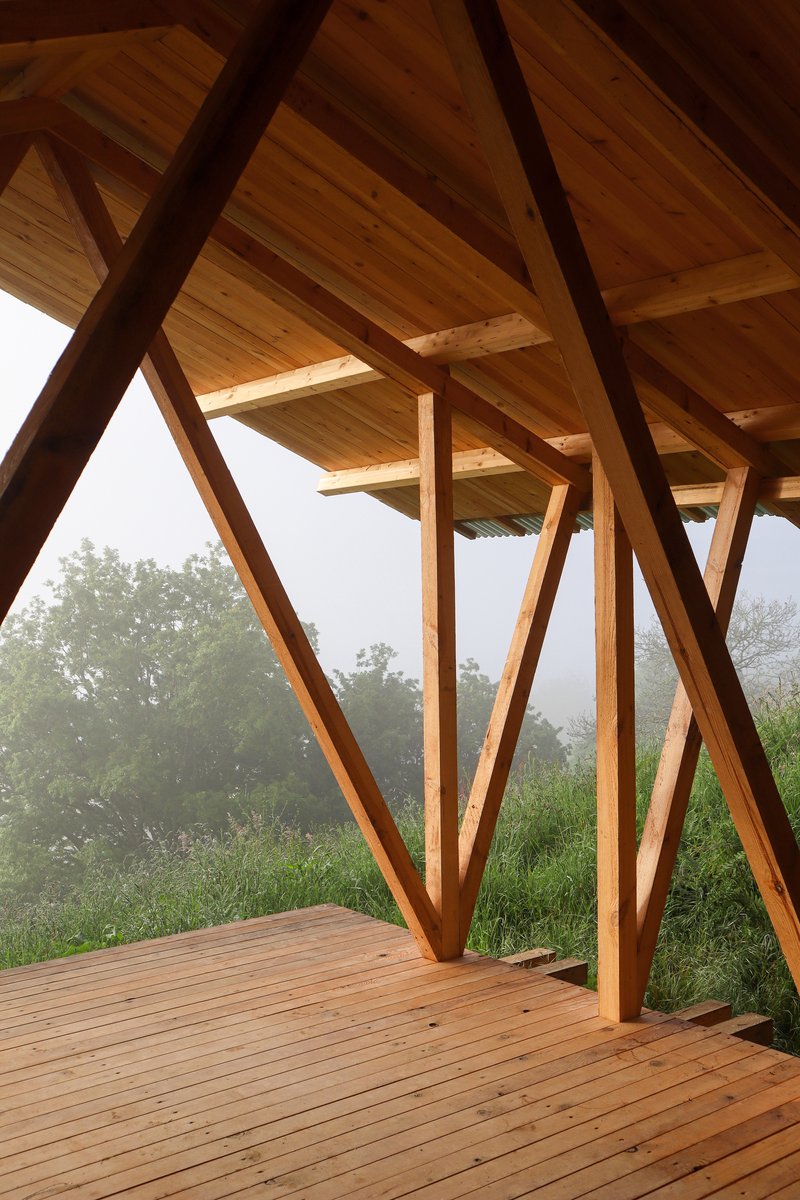 Interior view of the angled timber columns supporting wood plank ceiling with valley landscape visible through the opening