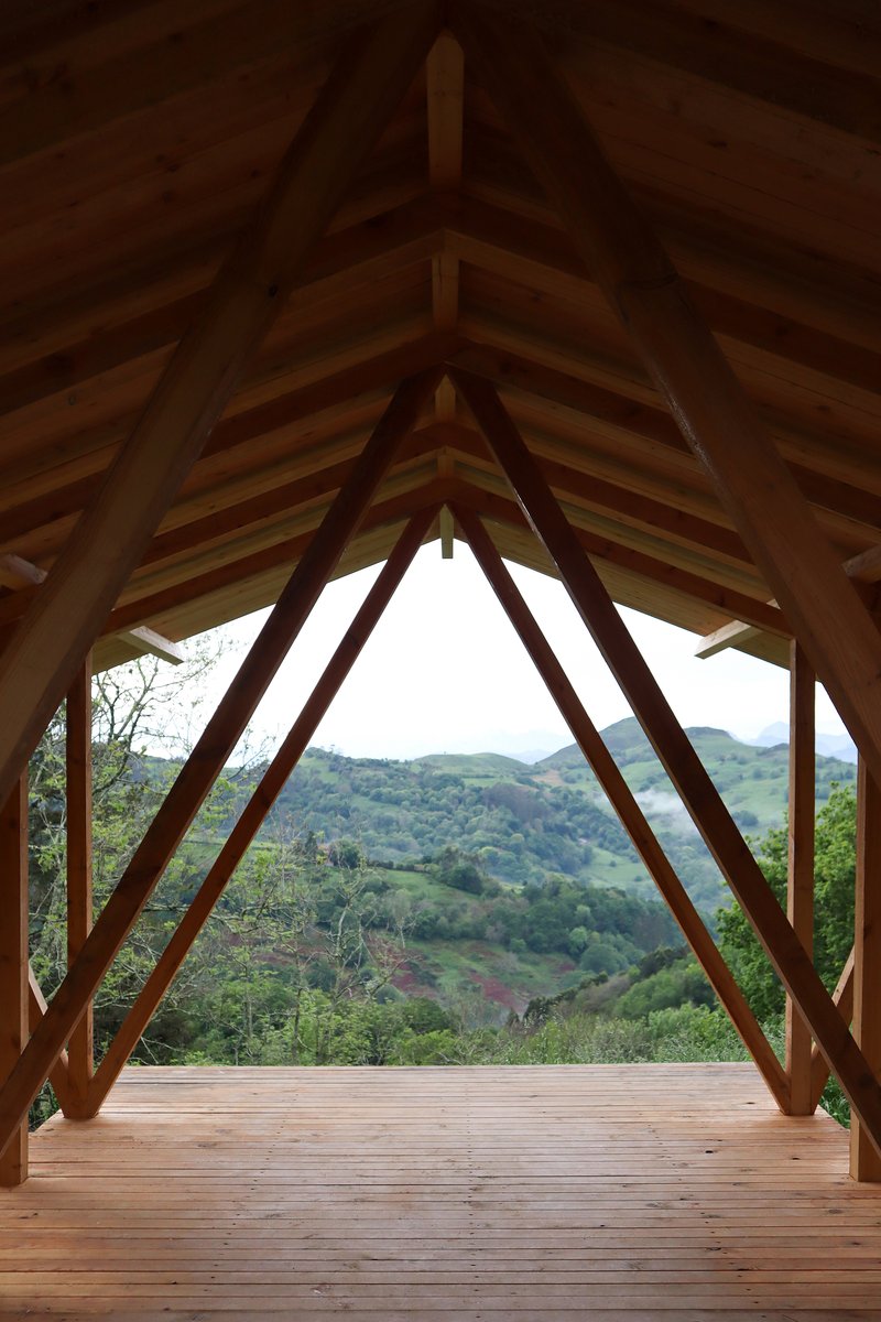 Interior view through the timber frame structure overlooking rolling green hills in the distance