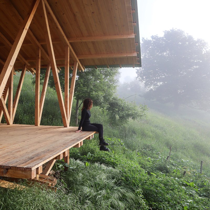 Person seated on the timber deck edge beneath the pavilion canopy in morning fog