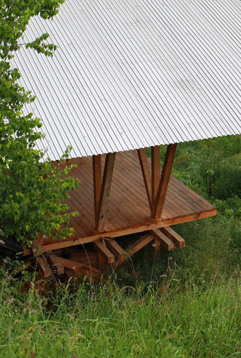 Aerial view of the corrugated metal roof and diagonal timber columns rising from the sloped terrain