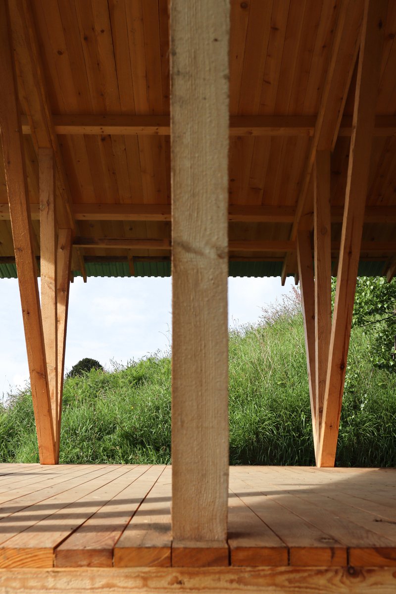 Wrapped column detail on timber deck beneath exposed rafter ceiling framing grassy slope beyond