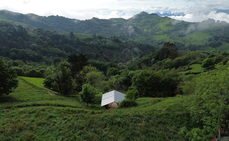 Small pavilion with white corrugated roof nestled in a valley among rolling green hills