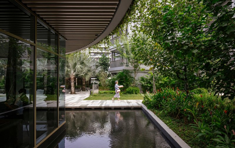 Covered walkway with timber slats beside a reflecting pool and planted courtyard with one person passing