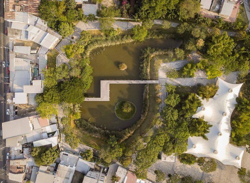 Overhead view of geometric water basins with circular island and white tensile canopy structure surrounded by vegetation