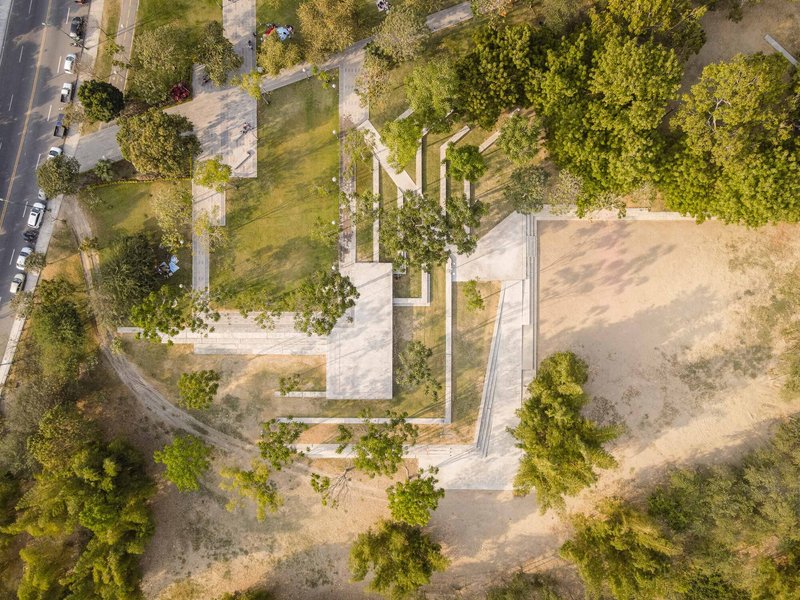 Drone view of a concrete pavilion with folded roof planes set among trees and lawn areas