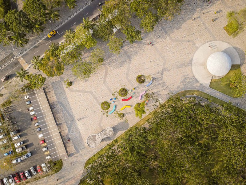 Overhead view of a public plaza with white spherical pavilion and multicolored seating elements beside a parking lot