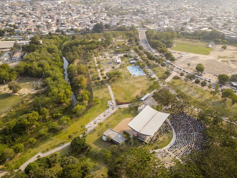 Aerial view of a cultural park showing amphitheater, white roof pavilion, and water features among tree canopy