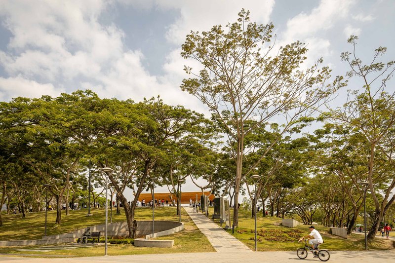 Park pathways leading to a distant pavilion with a cyclist passing and circular water feature
