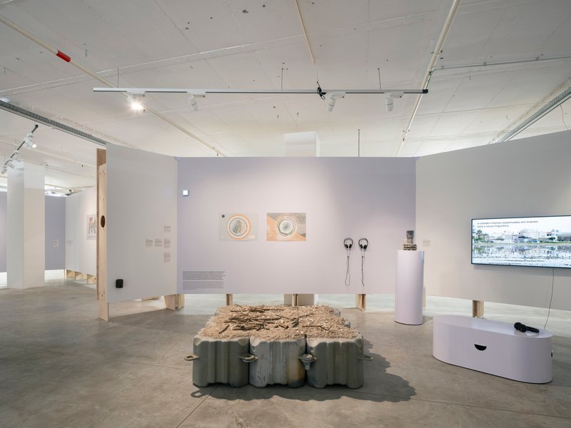 Gallery interior with white walls displaying artworks and a central table with textured surface under track lighting