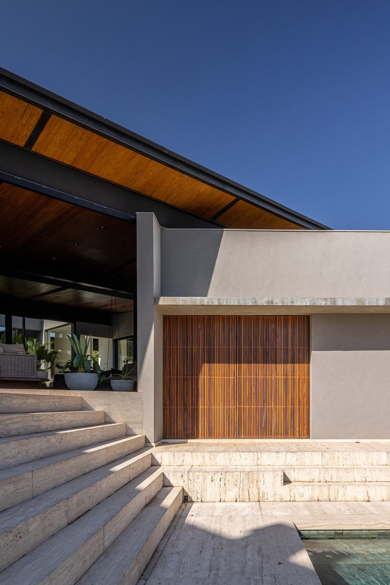 Stepped travertine terrace leading to timber-slat garage doors under cantilevered wood ceiling