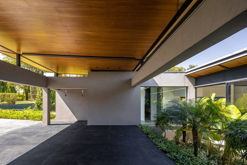 Covered entry carport with timber ceiling, concrete walls and planted bed beneath clerestory windows