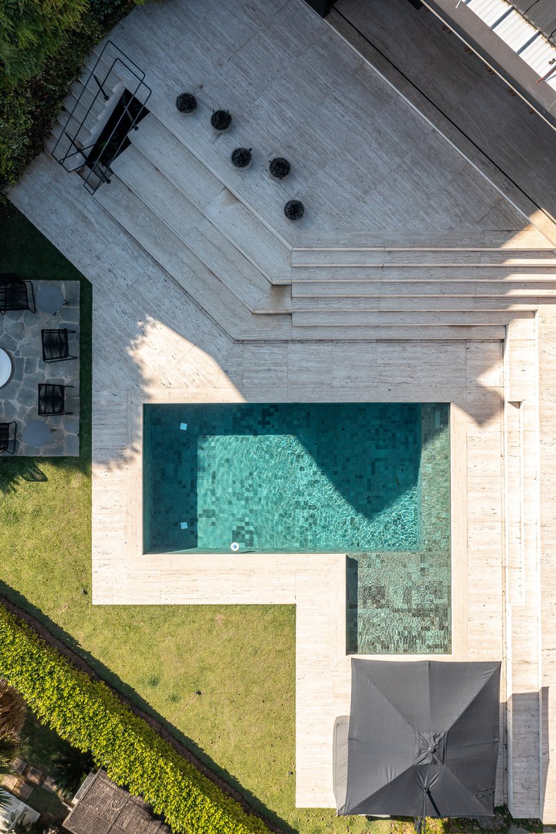 Aerial view of concrete deck with swimming pool and lawn courtyard in afternoon sunlight