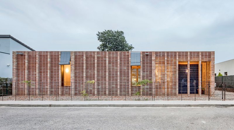 Street facade with layered brick walls and illuminated window openings at dusk