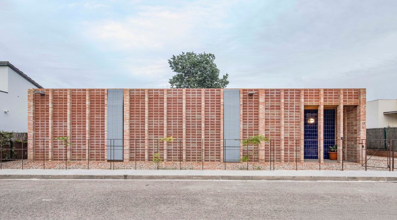 Street view of the perforated brick facade with vertical banding and a tree emerging from the roofline