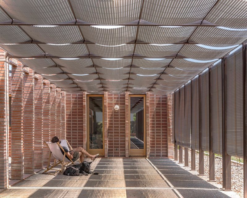 Covered porch with corrugated metal ceiling and perforated brick screens filtering afternoon light
