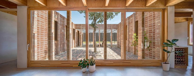 Timber-framed glazing overlooking a curved courtyard enclosed by perforated brick walls and gravel
