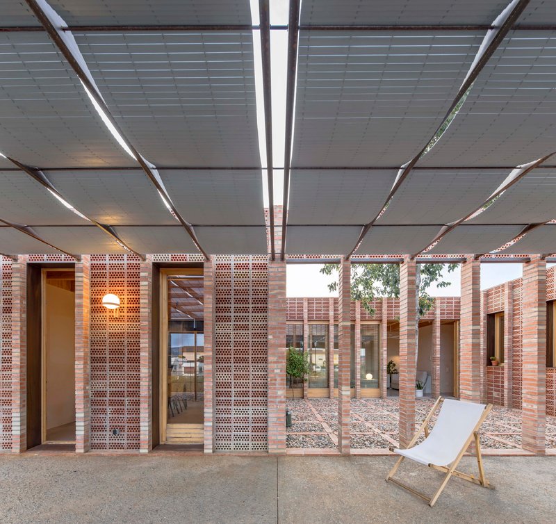 Covered porch with steel louvered canopy framing views of interior courtyard and perforated brick walls