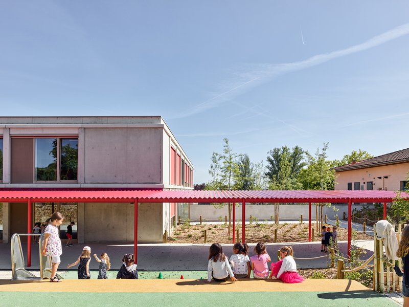 Outdoor play area with red canopy and children seated near a climbing mound under blue sky