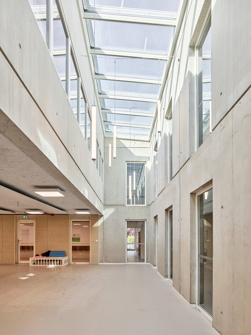 Skylit corridor with exposed concrete walls and timber-clad doorways beneath the glazed ceiling
