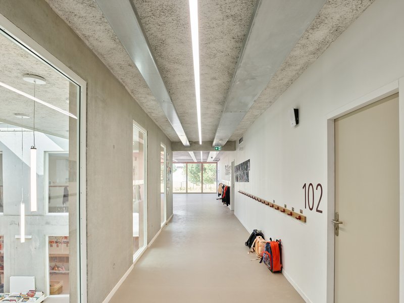 Upper-level corridor with glazed balustrade overlooking the atrium and coat hooks along the white wall