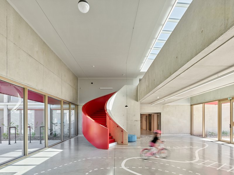 Red helical staircase connecting floors beside full-height glazing and concrete wall surfaces