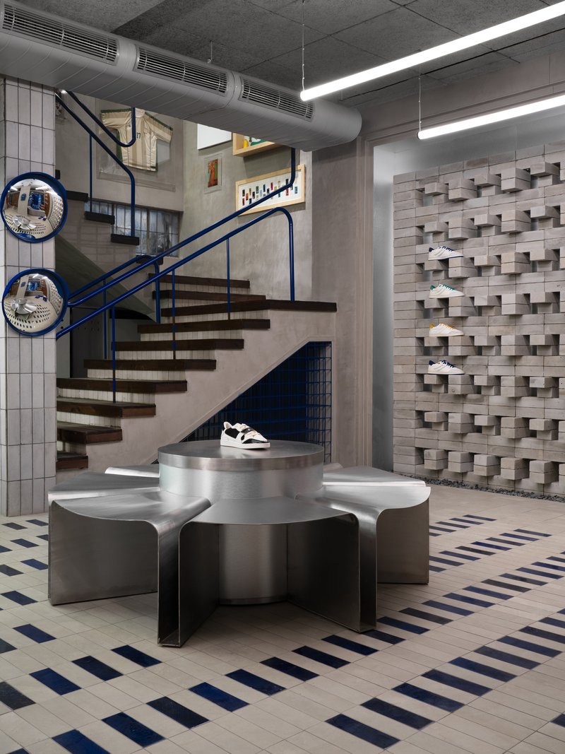 Floating timber stair with blue steel railing beside metal display pedestal and three-dimensional block wall
