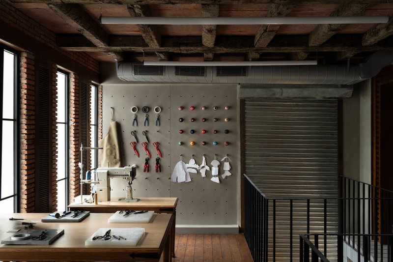 Upper level workspace with exposed timber beams, pegboard product wall, and louvered windows casting morning light