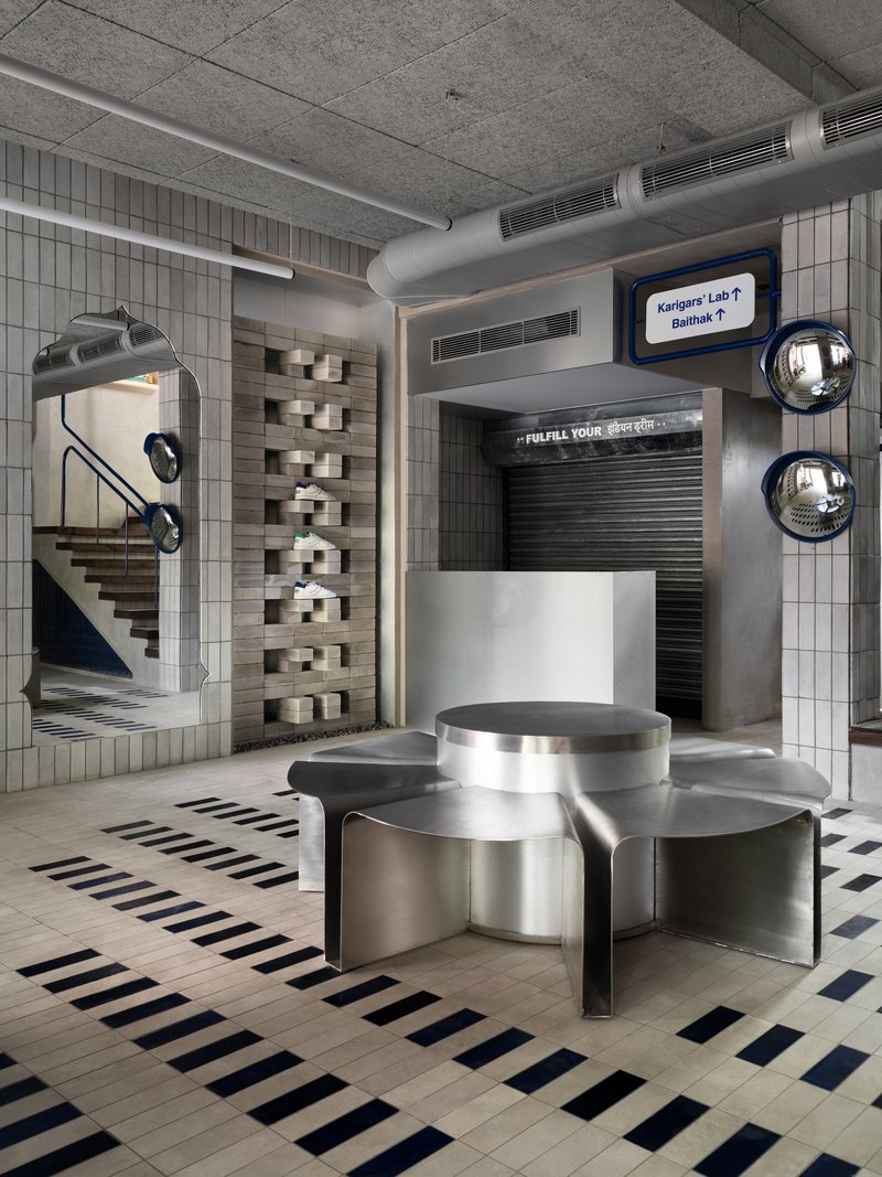 Interior retail space with stainless steel seating pod, striped floor tiles, and exposed concrete ceiling with mechanical ducts