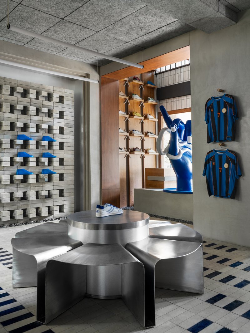 Stainless steel display table in front of timber-lined niche with merchandise and textured masonry wall