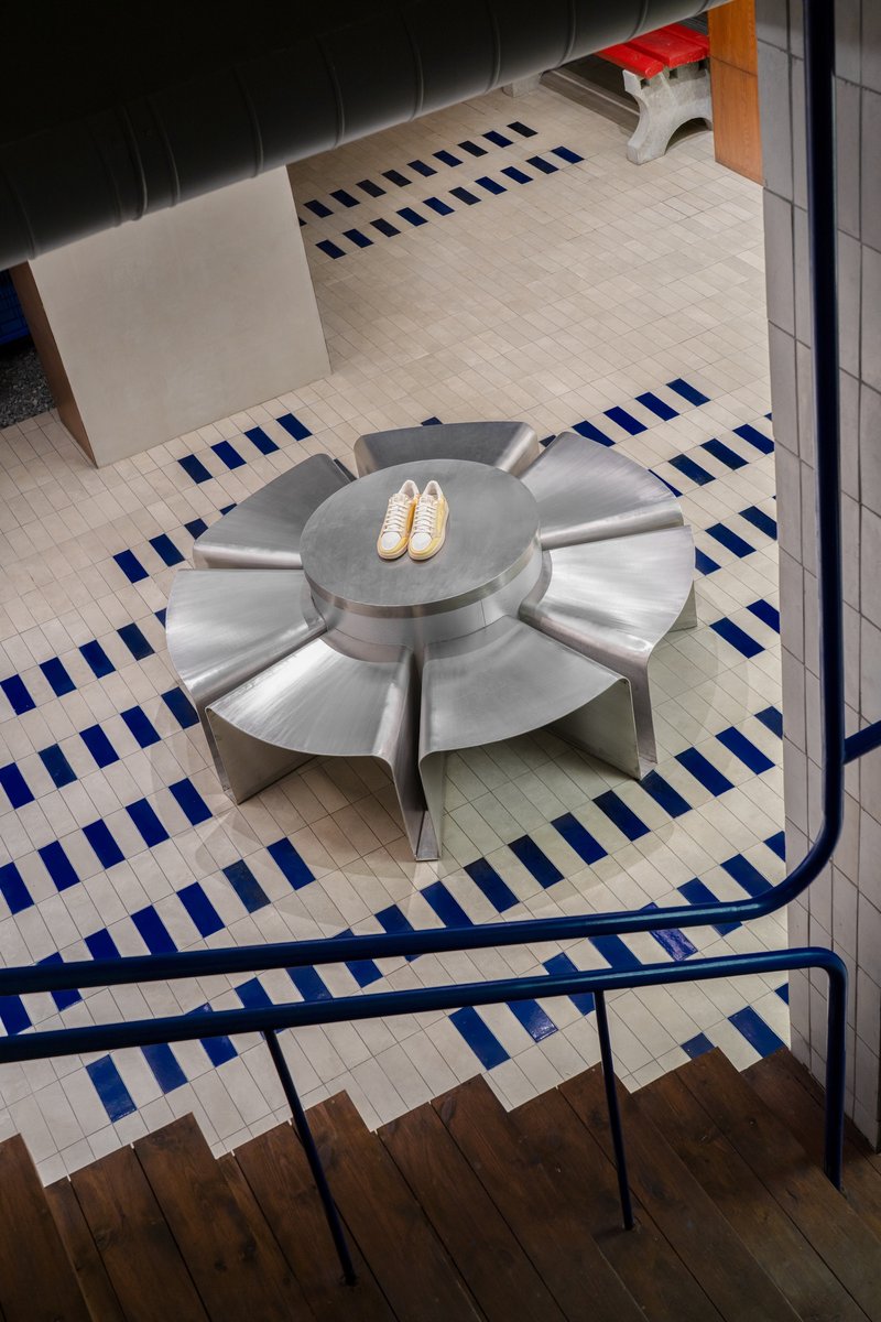 Looking down at stainless steel flower-shaped seating element on striped tile floor next to staircase