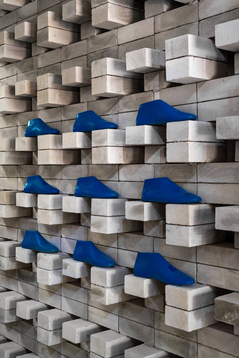 Close-up of staggered wood block wall with blue fabric footwear displayed on recessed ledges