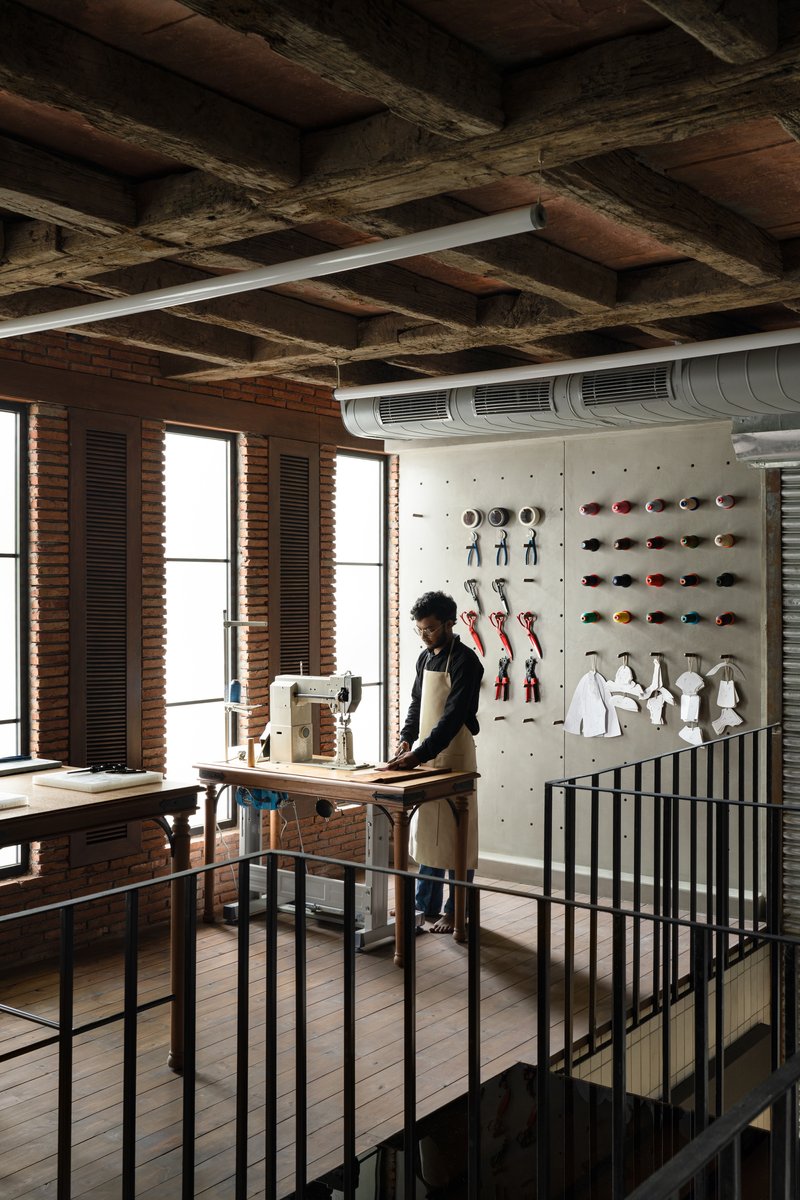 Upper level workspace with exposed timber ceiling joists and a person working at a cutting table