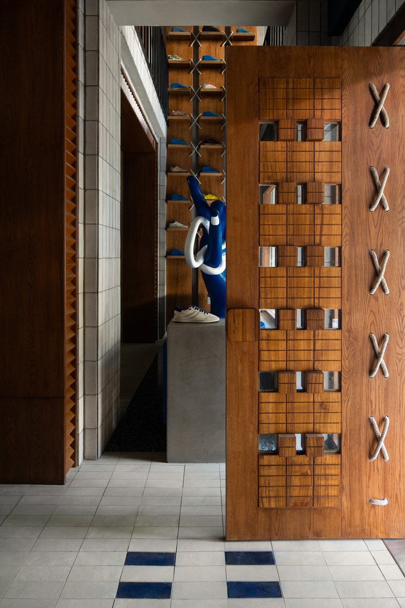 View down tiled corridor with blue sculpture and timber wall featuring rope crosses and grid display niches