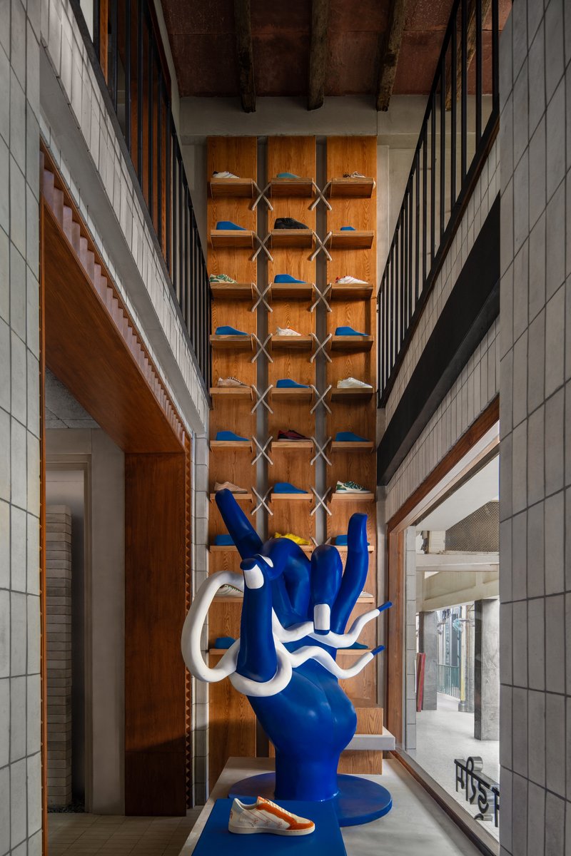 Double-height space with blue sculpture against timber wall and hexagonal shelving under exposed timber ceiling beams