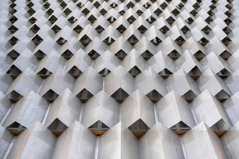 Close-up of textured concrete facade showing diamond-shaped projections with metal inserts creating a patterned surface