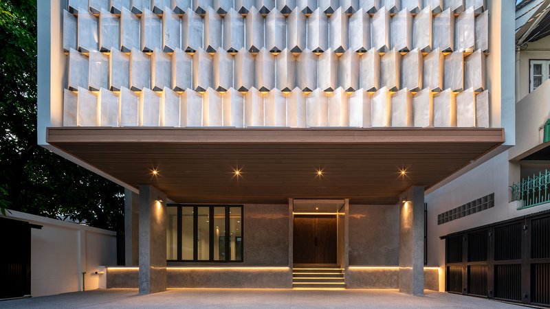 Street facade with cantilevered upper volume clad in concrete fins above an illuminated entry at twilight