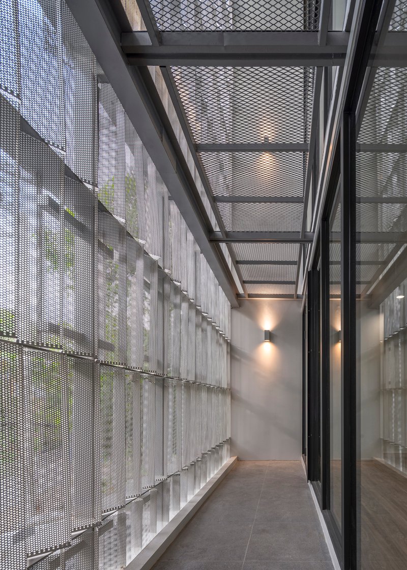 Narrow corridor with perforated metal screen wall and steel skylight structure overhead in diffused daylight