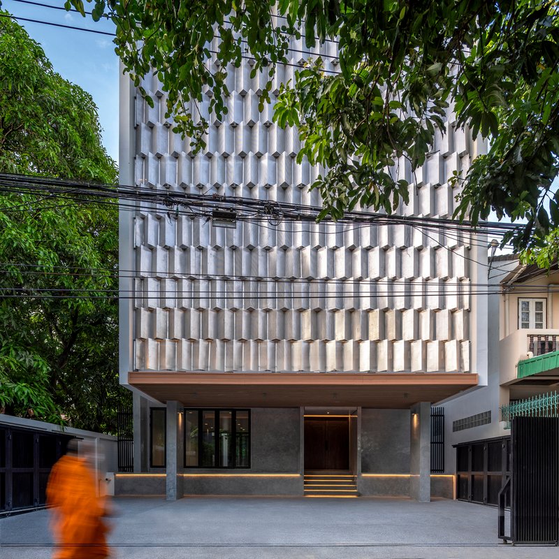 Street view of the white textured facade with overhead power lines and a pedestrian in motion