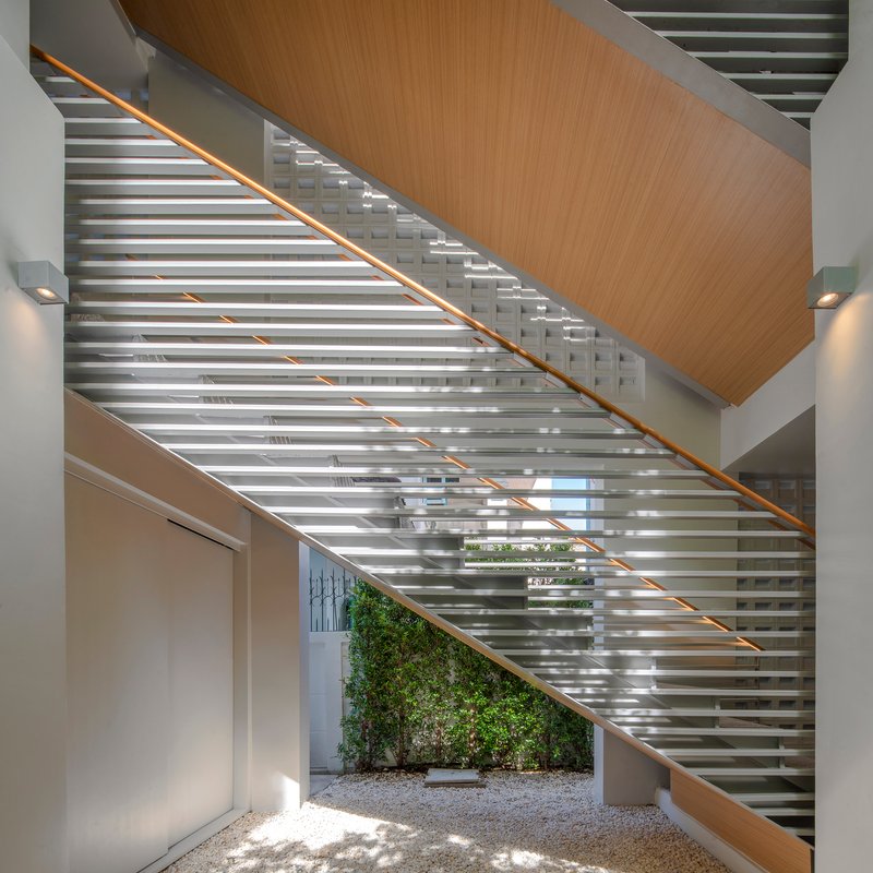 Steel staircase with timber handrail and underside overlooking a planted courtyard with gravel