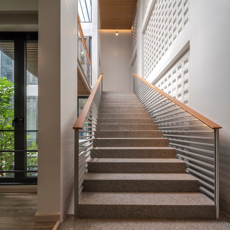 Terrazzo staircase with horizontal metal railings and timber handrails ascending toward a slatted timber ceiling
