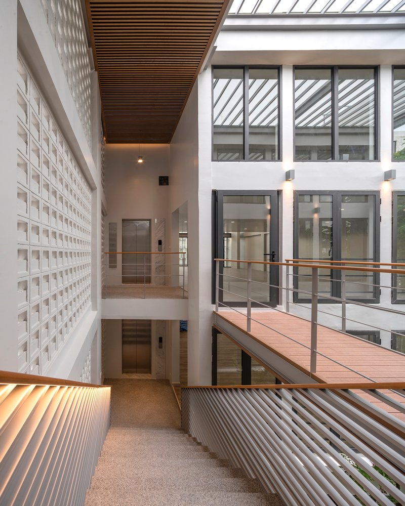 Upper level walkway with timber bridge connecting white perforated block walls under skylights