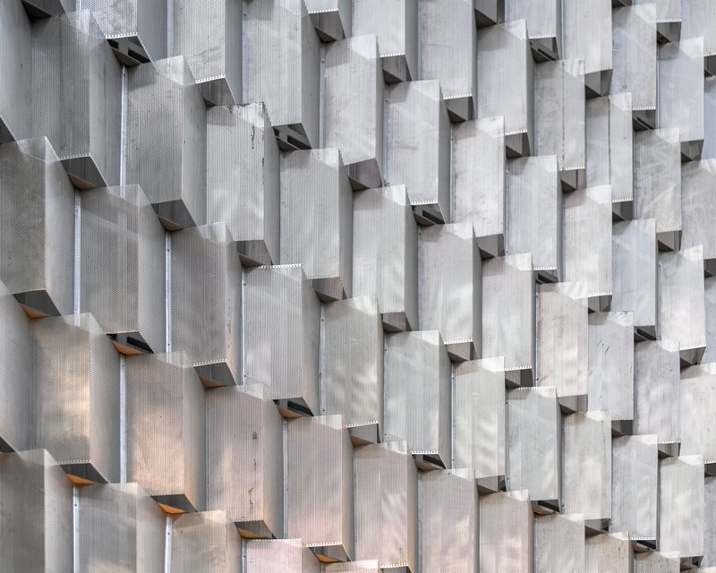 Facade composed of vertical precast concrete fins with folded metal ventilation openings in daylight