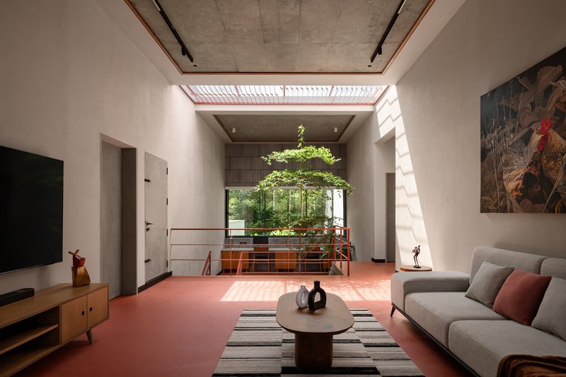 Living room with red resin floor looking toward interior courtyard tree under slatted skylight